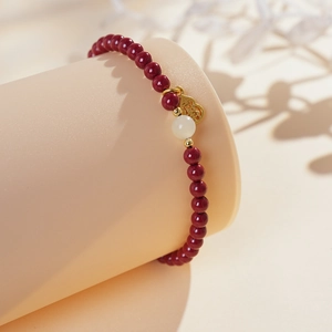 Detail view of red cinnabar bracelet with white bead and gold gourd charm on display