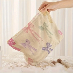 Beige corduroy cosmetic bag with colorful bow prints held in hand against curtains