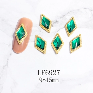 Detalle de dijes para uñas verde esmeralda de 9x15mm con borde dorado sobre mármol