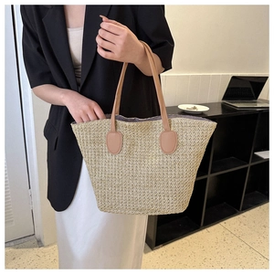 Detail of straw woven tote bag featuring brown leather handles and natural texture
