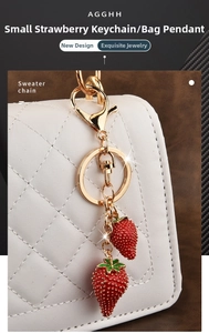 Detail view of two red strawberry charms with gold lobster clasp on a white bag