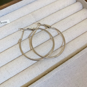Close-up of sleek silver hoop earrings resting on a beige velvet jewelry display tray