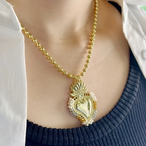 Detailed close-up of a gold Sacred Heart pendant with white beads on a beaded chain