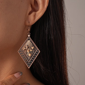 Macro detail of bronze diamond-shaped hollow earrings with ethnic beadwork on model