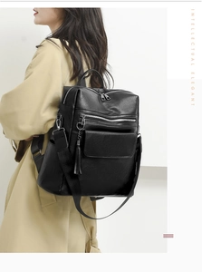 Fashionable black leather backpack with tassel detail worn over a stylish beige trench coat