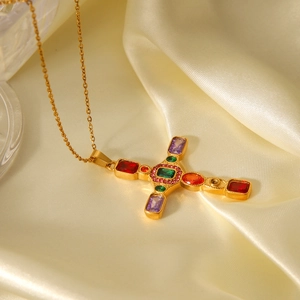 Close-up of golden cross pendant with colorful zircon stones on beige silk background