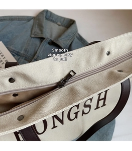 Detail of smooth metal zipper closure on a canvas tote bag with brown leather trim
