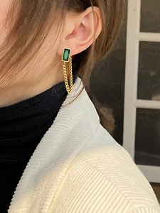 Detail of gold tassel earrings featuring a green rectangular crystal and delicate chains
