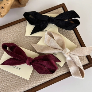 Three-piece velvet bow hair clips in black, burgundy and beige on a wooden display tray