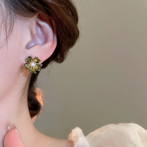 Detailed close-up of dark green flower stud earrings with diamonds on a model's ear