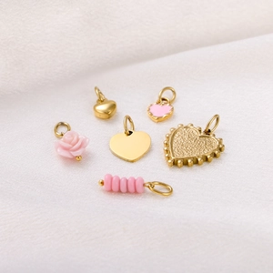 Detailed view of gold and pink heart pendants with rose charm on white silk fabric