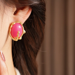 Gros plan d'une boucle d'oreille dorée en forme de corail avec pierre rose sur un modèle