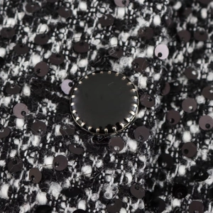 Close-up of black and white tweed fabric with sequins and a round metallic button