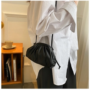 Detail of a black pleated dumpling crossbody bag worn by a model in a cozy indoor setting