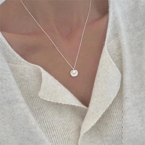 Detail of shell pendant necklace with pearl on a model wearing beige knitwear