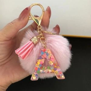 Close-up of pink pompom keychain with transparent letter A pendant and colorful heart sequins