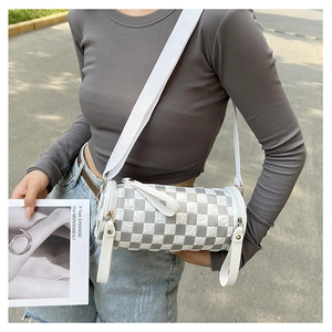 Checkboard cylinder crossbody bag with wide canvas strap shown in an outdoor lifestyle shot