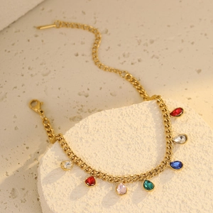 Detail of golden flat curb bracelet with colorful teardrop gemstone pendants on stone base
