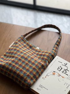 Detail of colorful plaid knitted shoulder bag with magnetic clasp on a wooden table