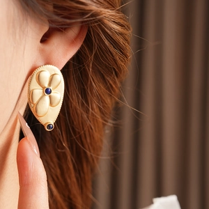 Close-up of vintage flower earrings in gold with round blue gemstone accents on model