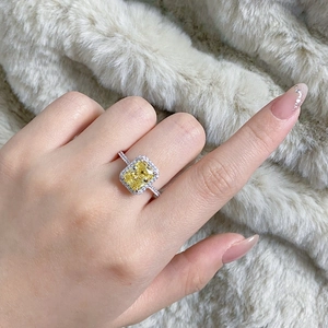 Detail view of a yellow radiant cut gemstone ring with halo diamonds on a hand