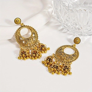 Detailed shot of golden Jhumka earrings with flower patterns and hanging bells on white silk
