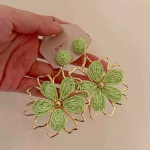 Detail of large hand-held green raffia flower earrings with golden openwork frame
