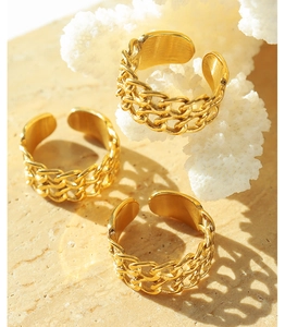 Three gold chain-link rings on white coral and textured stone with warm lighting