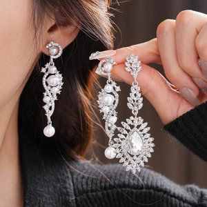 Detailed view of silver wheat pearl earrings with crystals worn by a model