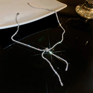 Detail of silver bowknot necklace with zircon stones on a dark reflective background