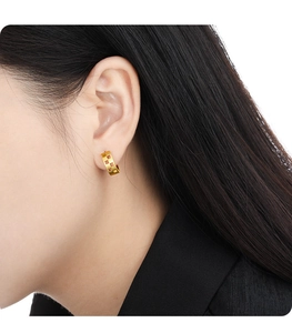 Close-up of golden geometric hollow-out hoop earrings on a model showing fine texture