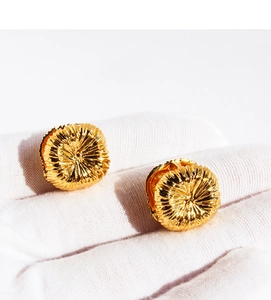 Close-up of golden artistic earrings with radiant pleated texture in a white gloved hand