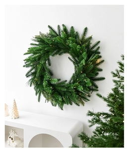 Detail of 60cm green Christmas wreath with warm LED lights hanging on a minimalist white wall