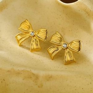 Eleganti orecchini a fiocco dorati con zircone in cristallo su vassoio in ceramica