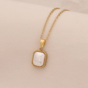Detailed view of a gold square pendant necklace with white stone inlay and beaded edges