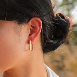 Polished two-tone rectangular stainless steel hoop earrings worn by a model in sunlight