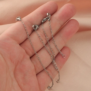 Three silver stainless steel extender chains with lobster clasps on a soft pink satin background