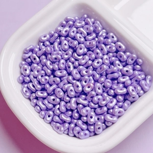 Macro detail of purple pearlescent peanut beads for DIY jewelry making in a white bowl