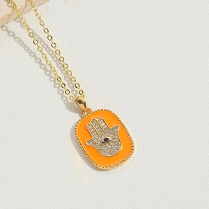 Macro shot of orange enamel Hamsa Hand pendant with zircon stones on golden chain