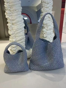 Blue-gray woven leather tote bag with a matching small pouch on a modern display
