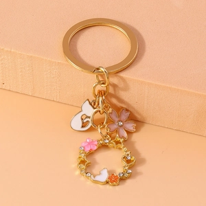 Detailed view of a gold keychain featuring a white cat, pink flower, and rhinestone wreath