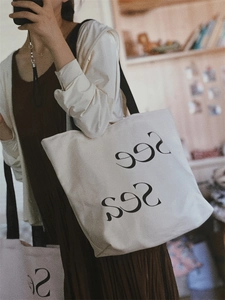 Detailed view of canvas tote bag featuring See Sea artistic lettering with comfortable shoulder strap