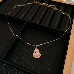 Close-up of a gold gourd pendant with pink cat eye stone in a black velvet jewelry box