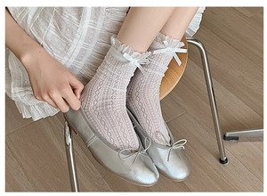 Close-up of white lace socks with ruffles and bows worn with silver ballet flats