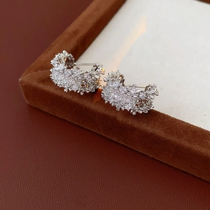 Macro shot of silver C-shaped earrings with micro-inlaid zircons on brown velvet tray