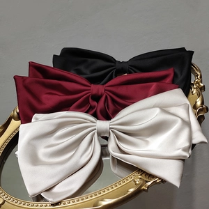 Elegant satin bow hair clips in black, deep red, and champagne on a vintage mirror
