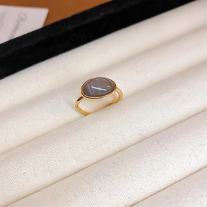 Detail eines vergoldeten Rings mit ovalem grauem Edelstein auf weißem Display