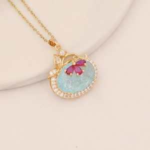 Detailed shot of golden necklace with light blue ice-cracked stone and red butterfly
