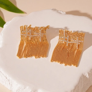 Golden tassel earrings with sparkling zircons on a white stone pedestal with leaves