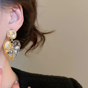 Close-up of vintage gold heart earrings with pearl and star details on model